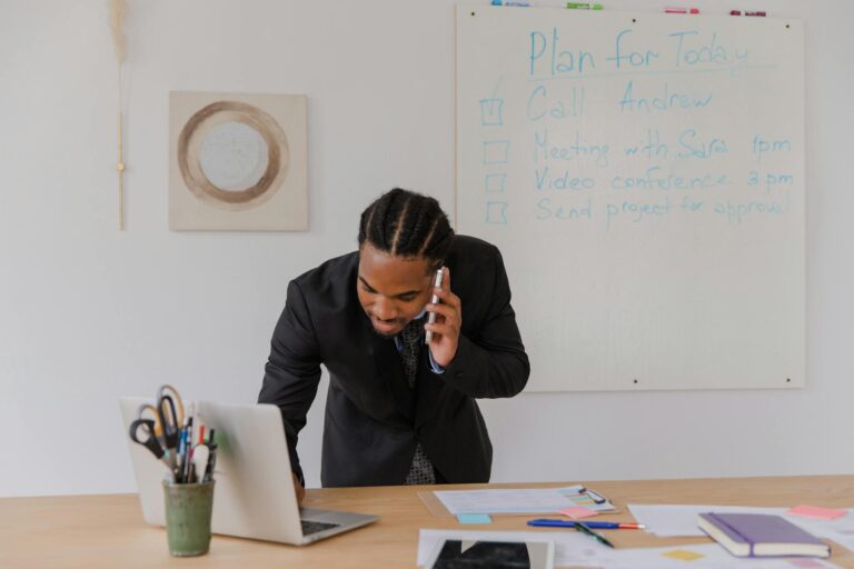 Businessman in an office making a call while working on a laptop with office supplies.